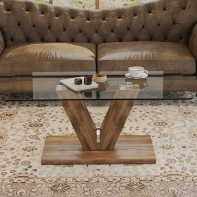 Une table basse de style minimaliste moderne. Plateau de table en verre trempé transparent avec colonnes en bois aggloméré. Convient au salon et à la salle à manger