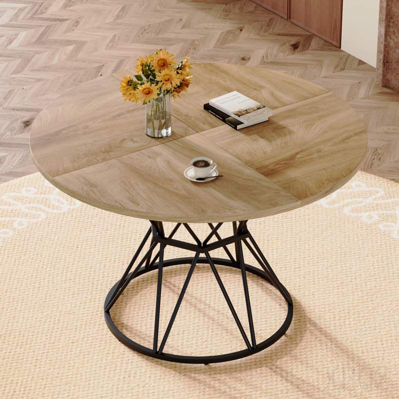 Une table de salle à manger circulaire d'un diamètre de 47,3 pouces, comprenant 4 plateaux de table en MDF à grain de bois clair, des supports en métal en forme de sablier noir et une table de salle à manger de style industriel moderne pour 4 à 6 personnes.