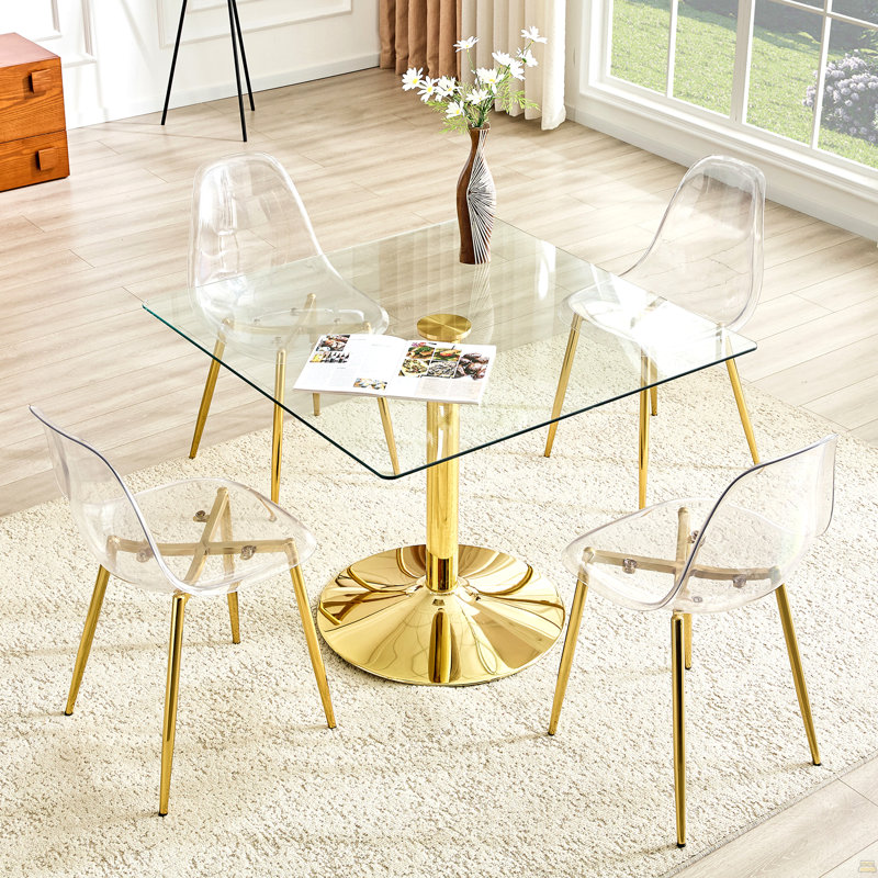 Ensemble de table et de chaises Table de salle à manger carrée en verre minimaliste moderne de 38,5 pouces avec base en métal doré. Comprend 4 chaises en plastique transparent avec pieds en métal doré.