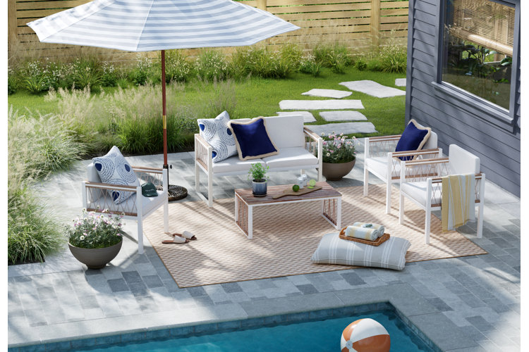 modern coastal poolside patio with a patio conversation set, jute area rug, and a striped market umbrella