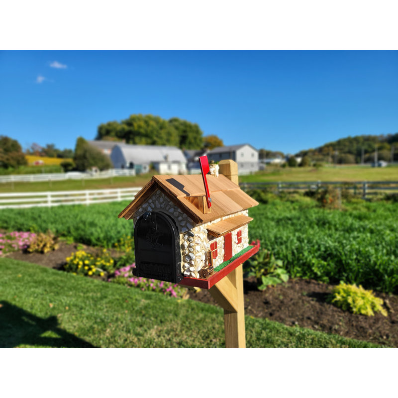Handmade barn-style mailbox with a stone exterior, cedar shake roof, and red flag mounted on a wooden post.