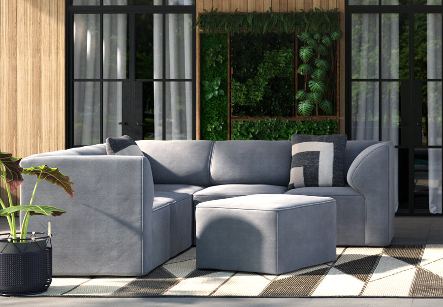 A gray patio sectional with a square ottoman outside. There's a planter next to the sectional and it is on a brown and white outdoor rug.