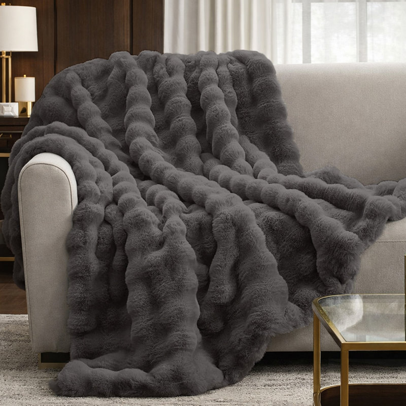 Dark gray faux fur throw blanket with a textured bubble wave design draped over a beige sofa.