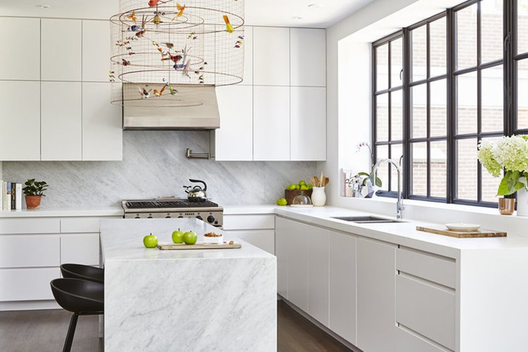 A clean white modern kitchen with pops of green and a decorative chandelier with colorful birds.