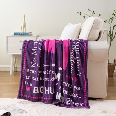 Purple throw blanket with white printed heartfelt messages and heart icons draped over a white sofa.