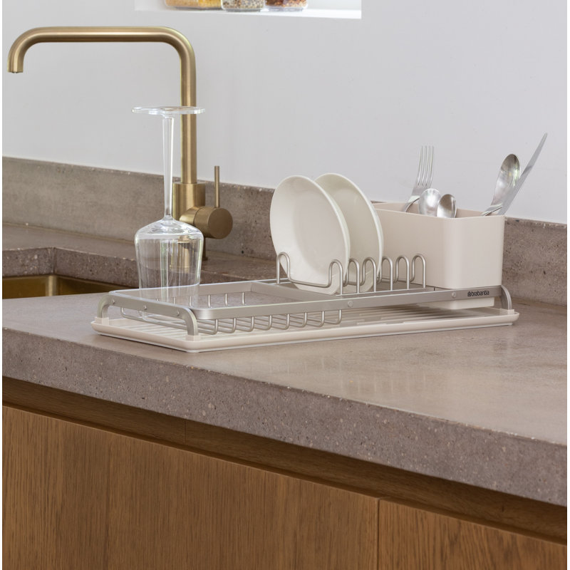 Compact gray aluminum dish drying rack with a removable cutlery caddy, holding plates and a wine glass on a kitchen counter.