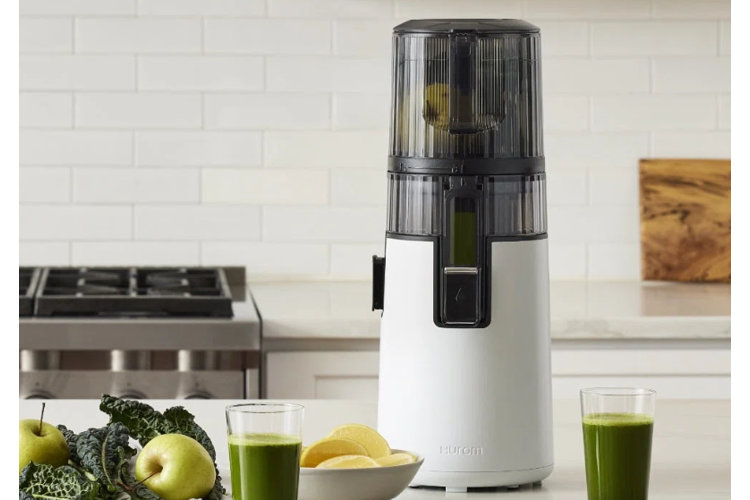 white masticating juicer on kitchen counter with glass of green juice
