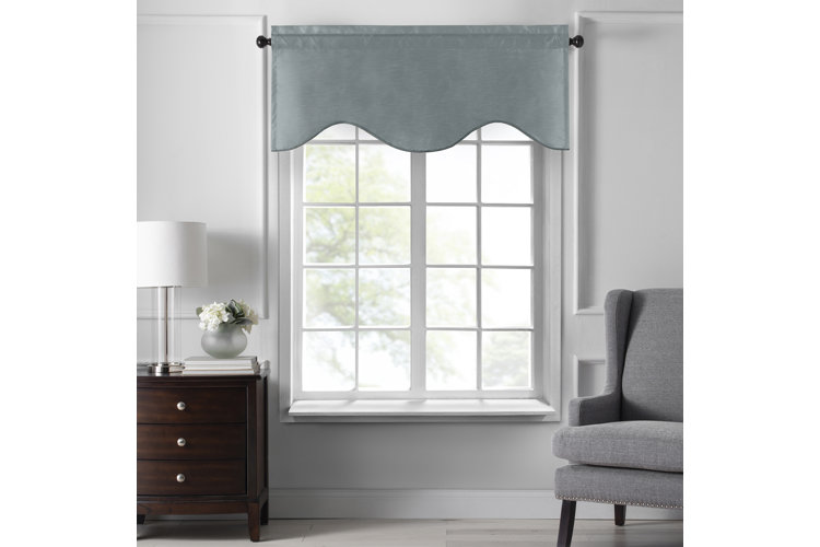 blue scalloped valance over a big window. next to the window is a gray accent chair and a brown, wood nightstand with a glass lamp on top of it