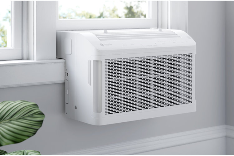 A white GE Profile saddle window air conditioner installed in a window frame, with the main body hanging below the window sill inside the room.
