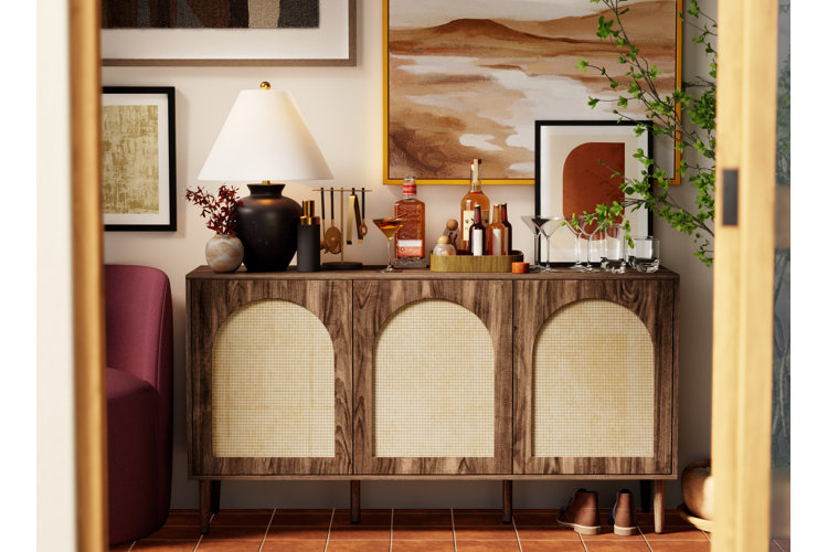Small space home bar on a credenza in a passageway. Various bar tools, alcohol bottles, and glasses next to a black lamp
