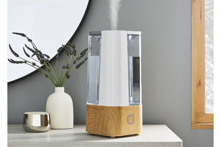 white and wood-look humidifier on a dresser beside a white vase and silver candle