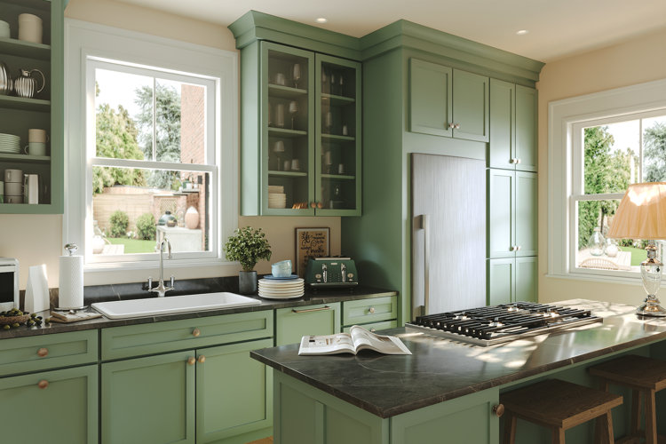 Green painted kitchen with a black marble countertop island featuring a stove. Large white sink beneath a window surrounded by plenty of cabinets for kitchen essentials