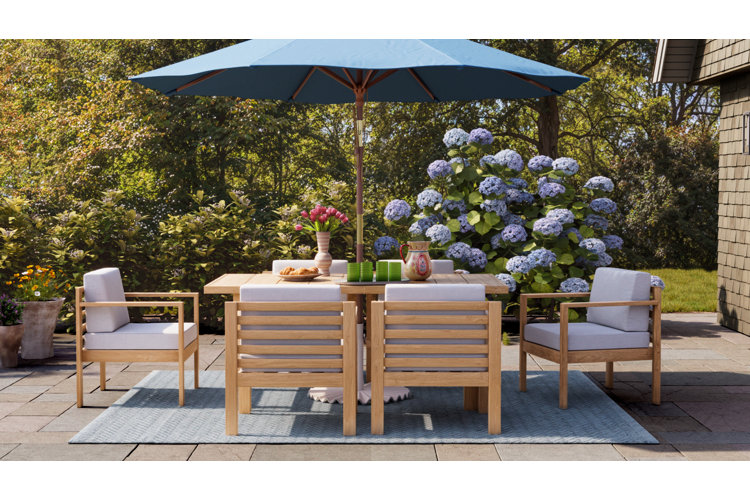 wood patio furniture dining set with a blue outdoor umbrella on a patio surrounded by grass and trees for how to find the best outdoor furniture