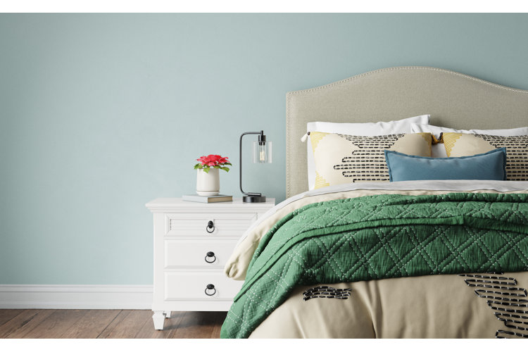 bedroom with light blue walls, an upholstered bed, beige comforter, and dark green coverlet across the bottom of the bed.
