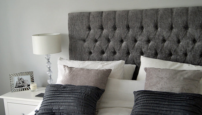 brand new pillows, a luxurious tufted headboard, and a bedside table with photo frames and candles