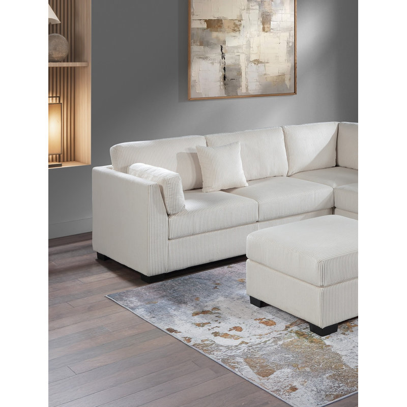 Canapé d'angle en velours côtelé beige en forme de L avec accoudoirs, coussins et pouf de cocktail