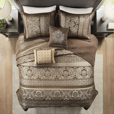 Couvre-lit réversible 5 pièces pour grand lit. Brun et or. Comprend un couvre-lit, 2 taies décoratives et des coussins décoratifs. Fait de luxe durable. Présente des feuilles, des rayures et des motifs. Accentué par des coutures. Or