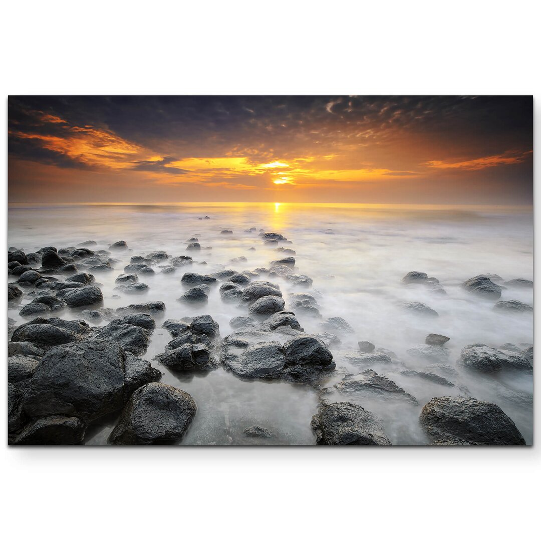 Leinwandbild Sonnenaufgang über einem Strand mit schwarzen Steinen