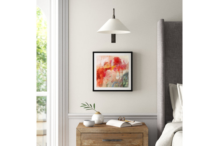 Close up of beside a bed, with a red watercolor-abstract painting hanging above the nightstand.