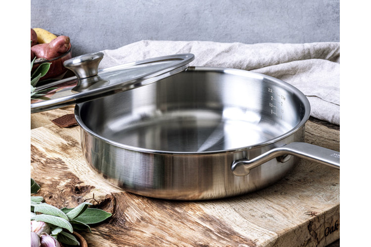 stainless steel sauté pan on a wood chopping board next to fresh sage, garlic, and potatoes
