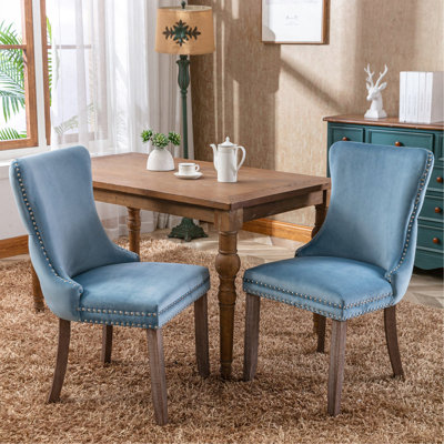 Luxueuse chaise de salle à manger rembourrée en velours avec dossier haut et garniture cloutée exquise, offrant un confort supérieur et un style élégant.