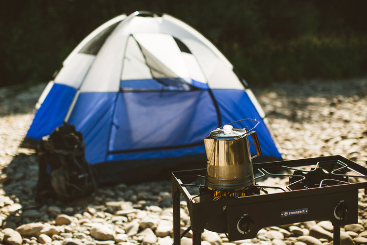 metal percolator on camping stove in front of tent