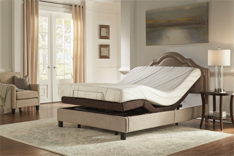 An adjustable bed with a tan upholstered bedframe and a foam mattress