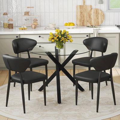 Ensemble de table et de chaises. Table ronde moderne en verre: support en métal noir en forme de X de 31 pouces de diamètre. Jumelé avec 4 chaises de salle à manger ergonomiques en polyuréthane noir, avec un dossier incurvé pour une conception confortable.