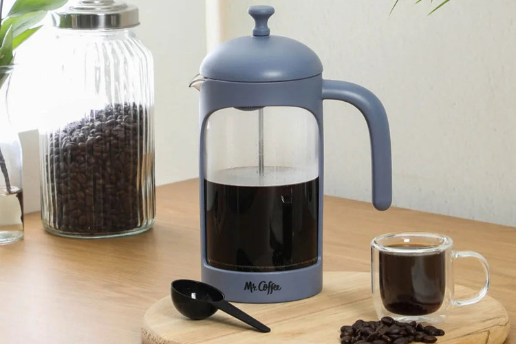 blue Mr. Coffee French press on a wooden tray with a glass mug of coffee and a canister of whole coffee beans