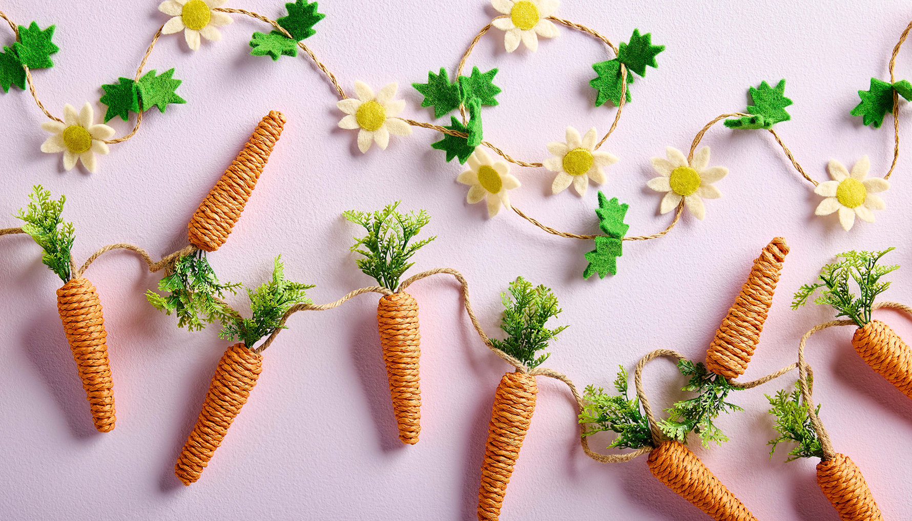 Guirlande de marguerites et de carottes sur fond rose.