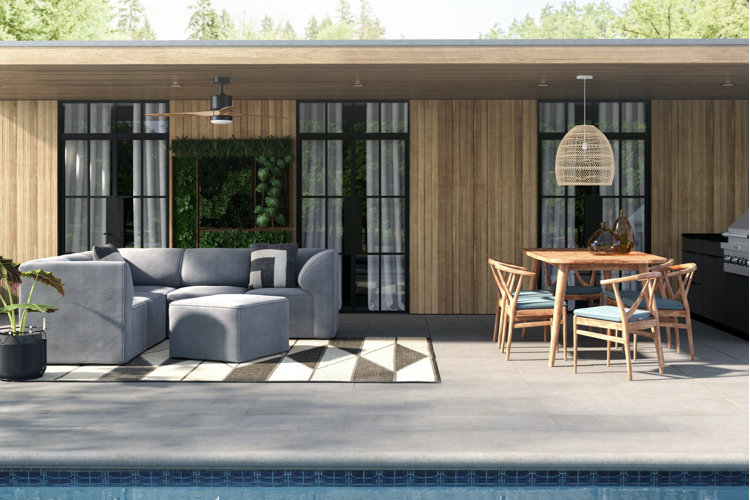 Poolside patio up against a wood paneled house with an overhanging roof above an outdoor sectional sofa and dining set.