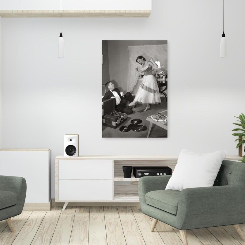 1950S 1960S Teen Couple In Living Room In Prom Dress & Tuxedo Guy Sitting On Floor & Girl Dancing To Music From A Record Player Romantic Contempora...