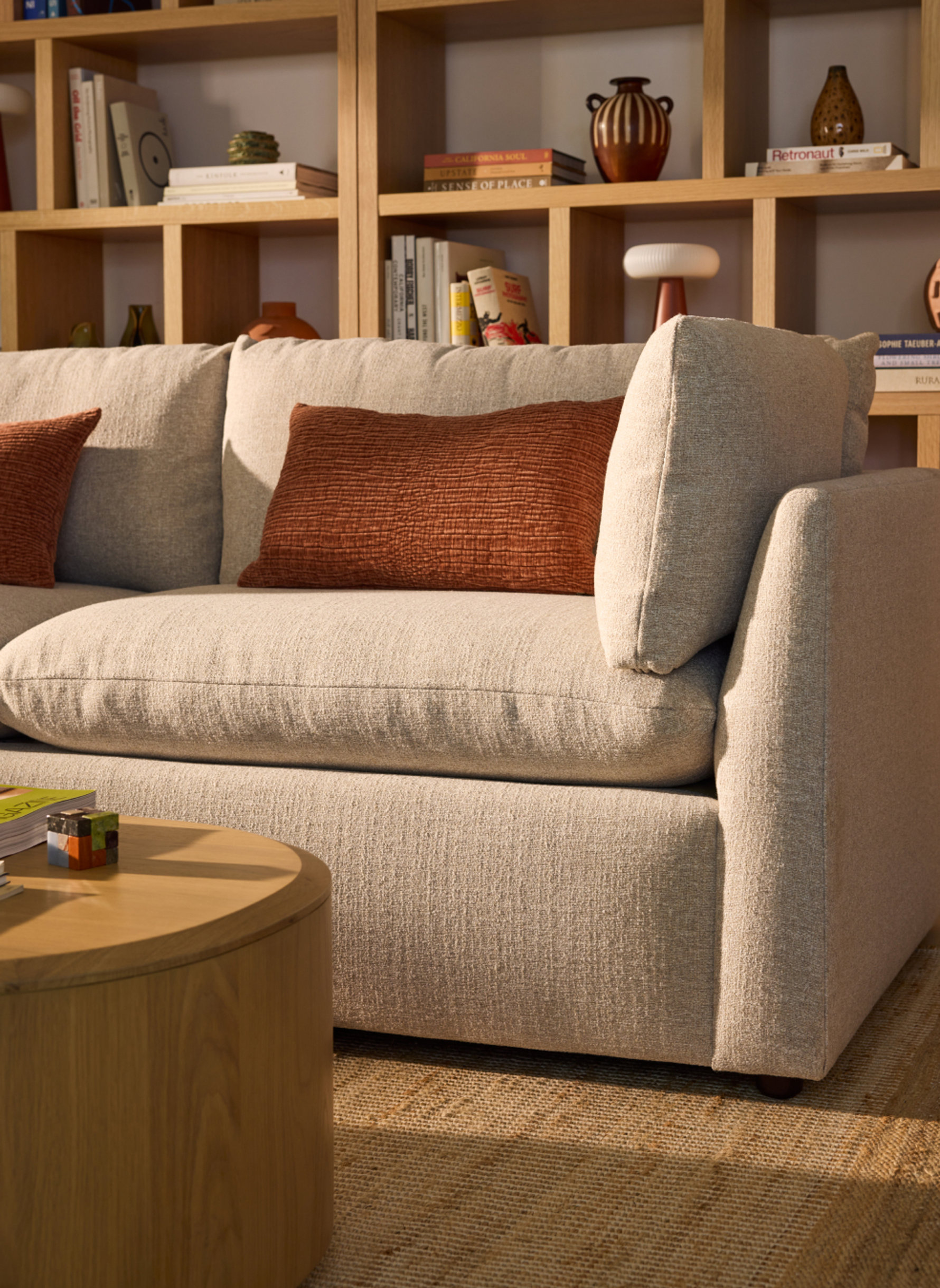 Close-up of a light-colored sofa with burnt orange pillows and wooden bookshelves in the background.