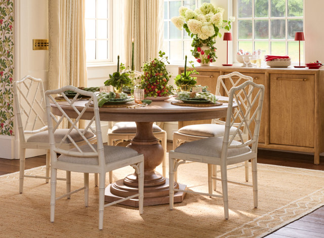 Round wooden dining table with a pedestal base and off-white bamboo-style chairs in a bright, sunlit dining room.