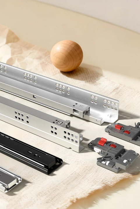 Silver and black metal drawer slides with gray mounting hardware arranged on a textured surface next to a wooden sphere.