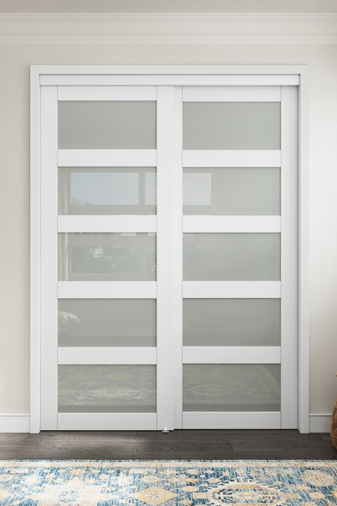 White double sliding closet doors with five horizontal frosted glass panels set against a neutral wall with a patterned blue rug in the foreground.