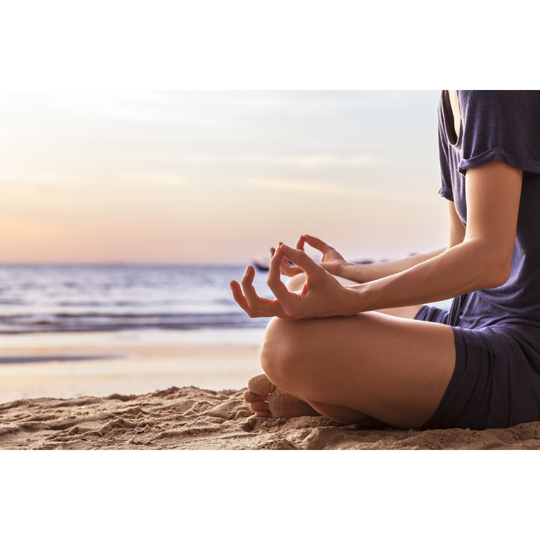 Leinwandbild Junge Frau übt Yoga am Strand bei Sonnenuntergang