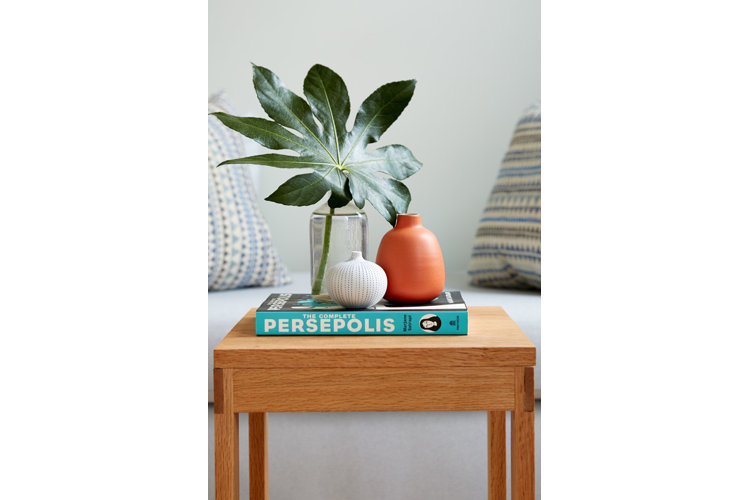An end table with a palm leaf in a vase and white and terracotta ceramics.