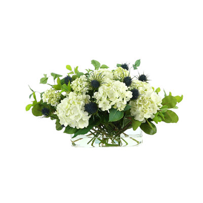 Arrangement floral d'hortensias et de chardons dans un vase en verre rectangulaire
