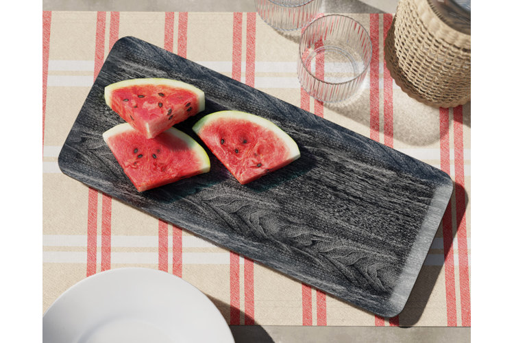 Patio table with a red stripe table runner and a gray wood tray used to display sliced watermelon.