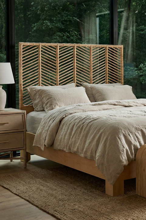 Natural light bedroom featuring a wooden bed frame with a tall woven rattan headboard in a chevron pattern, styled with beige linen bedding, a bedside table, and a neutral area rug against a backdrop of floor-to-ceiling windows.