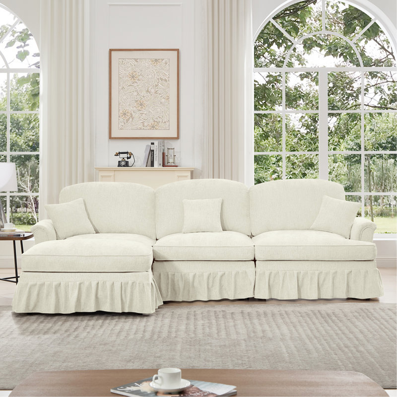 Canapé trois places de style années 50 avec accoudoirs évasés, jupe à volants amovible et plissée, tissu chenille beige et blanc, confortable, modulable et détachable.