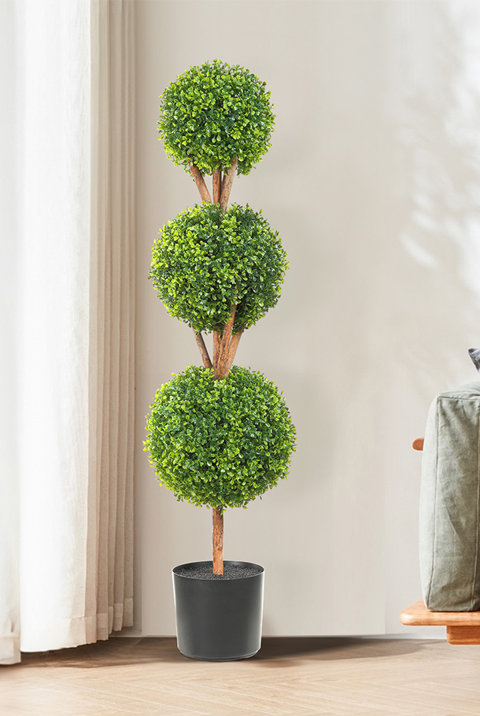 Artificial triple-ball boxwood topiary tree in a black pot standing in a bright living room.