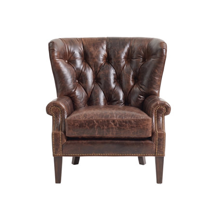 Brown leather wingback armchair with button tufting and nailhead trim on wooden legs.