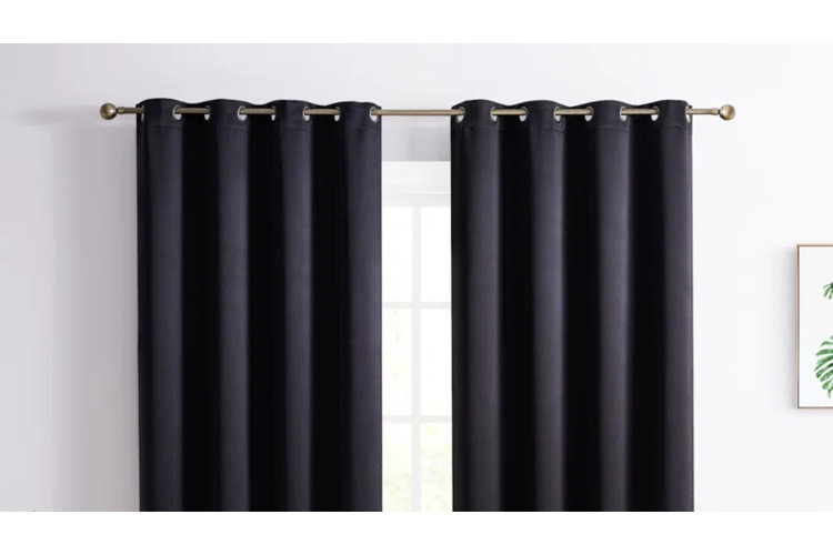 Black grommet blackout curtains hanging on a gold rod against a white wall