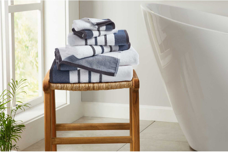 stack of striped blue and white towels and washcloths arranged on woven wooden stool beside bathtub