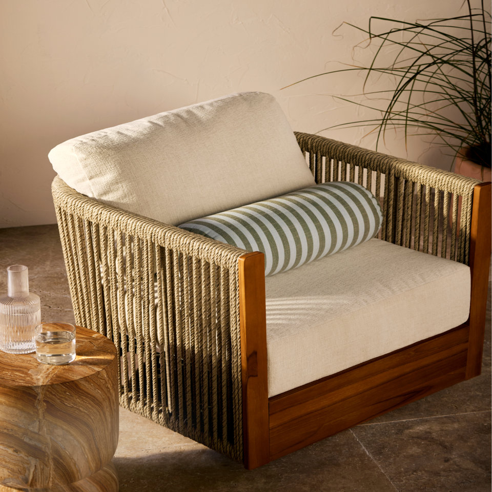 Upholstered rope armchair with striped bolster pillow.