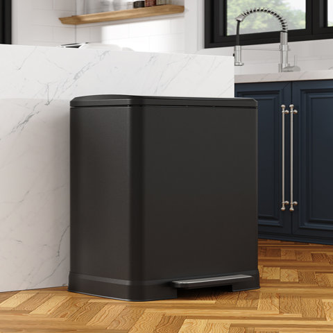 Matte black rectangular kitchen trash can with a pedal-operated lid situated on a wood floor next to a white marble kitchen island.