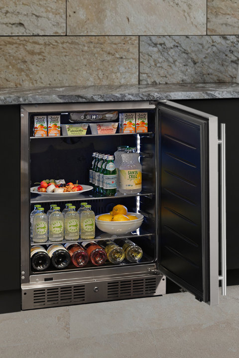 Stainless steel undercounter refrigerator with open door, stocked with juice boxes, bottled sparkling water, fresh fruit, and wine bottles.