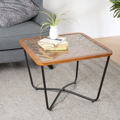 Table basse carrée élégante avec dessus en verre découpé géométriquement et structure en fer robuste pour un aspect vieilli. Plateau en verre trempé, cadre en métal noir, montage facile.
